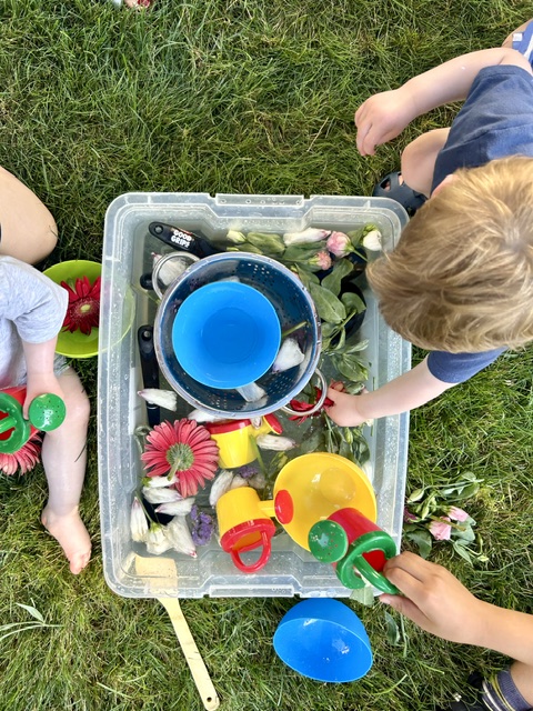 Children playing with flowers and scoops in a water bin