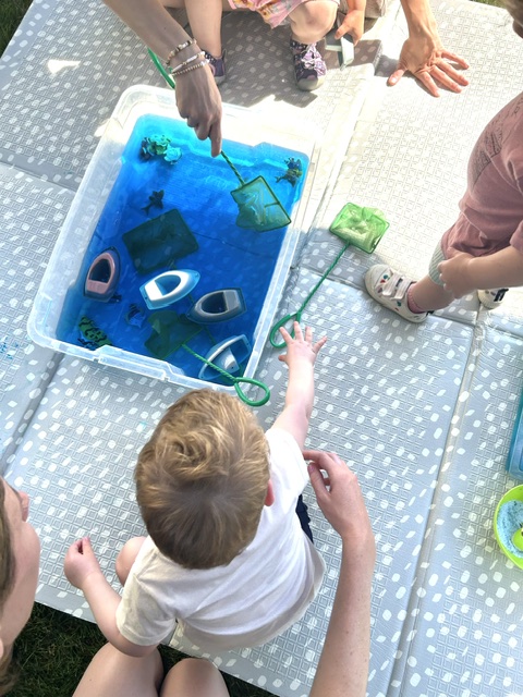 Child reaching into a blue ocean sensory bin with toy boats