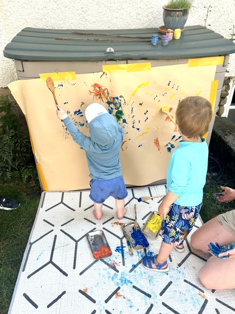 Children painting a cardboard box mural outdoors