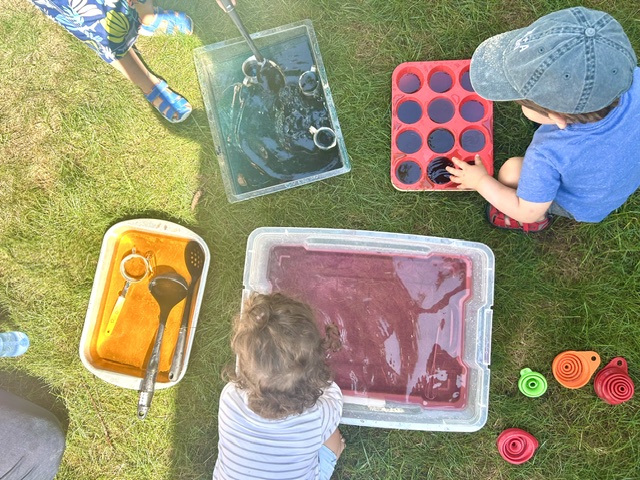 Two children at a colorful water and muffin tin sensory station